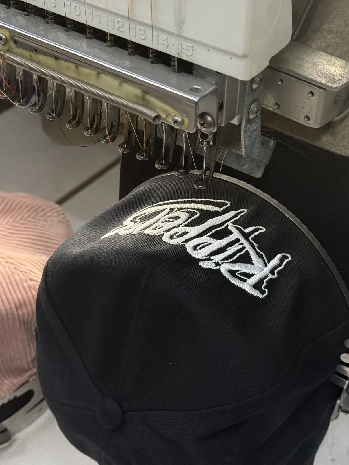 A black cap under the needle, script stitching out on the embroidery machine
