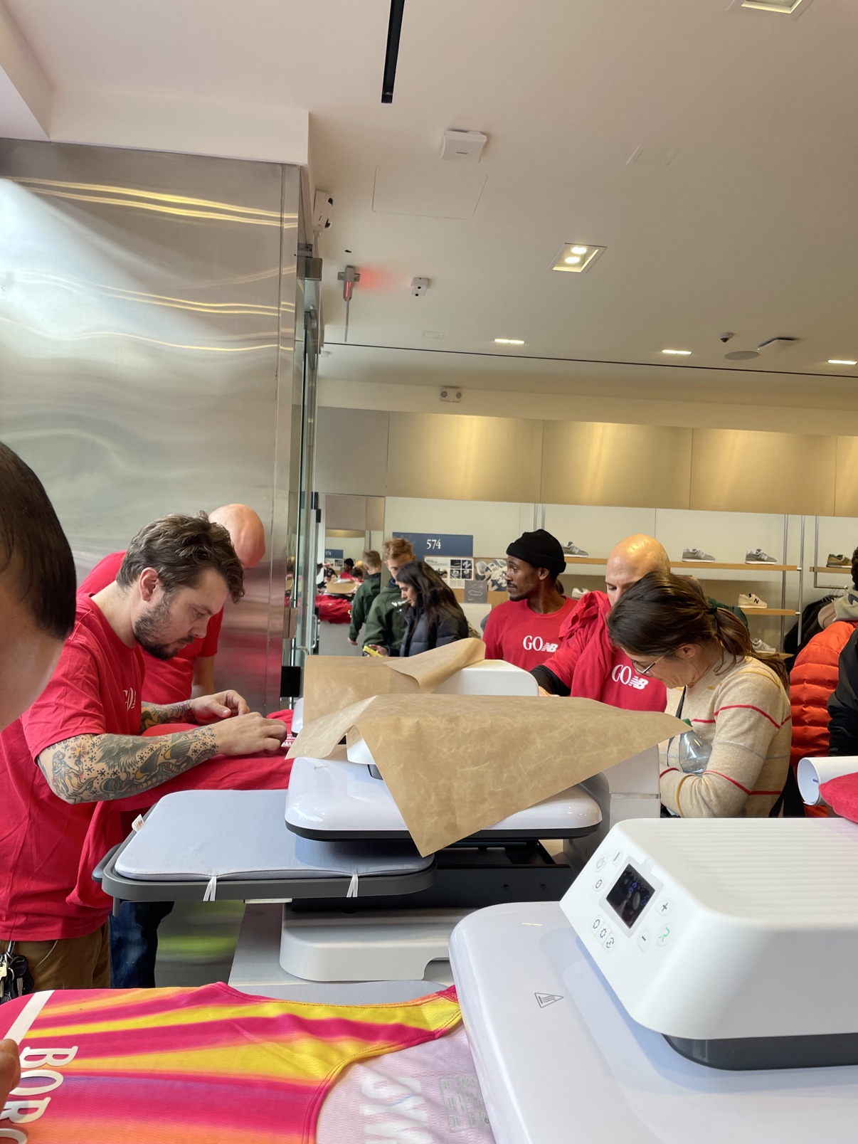 Heat press line running inside the New Balance store, crew pressing singlets for guests